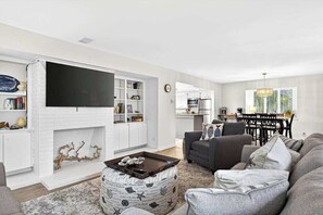 Ein Wohnzimmer mit Flachbildfernseher, Kamin, Essbereich und Küche.