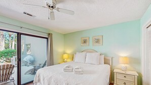 Ein Schlafzimmer mit einem Bett, zwei Nachttischlampen, einem Deckenventilator und einer Glastür, die zu einem Außenbereich führt.