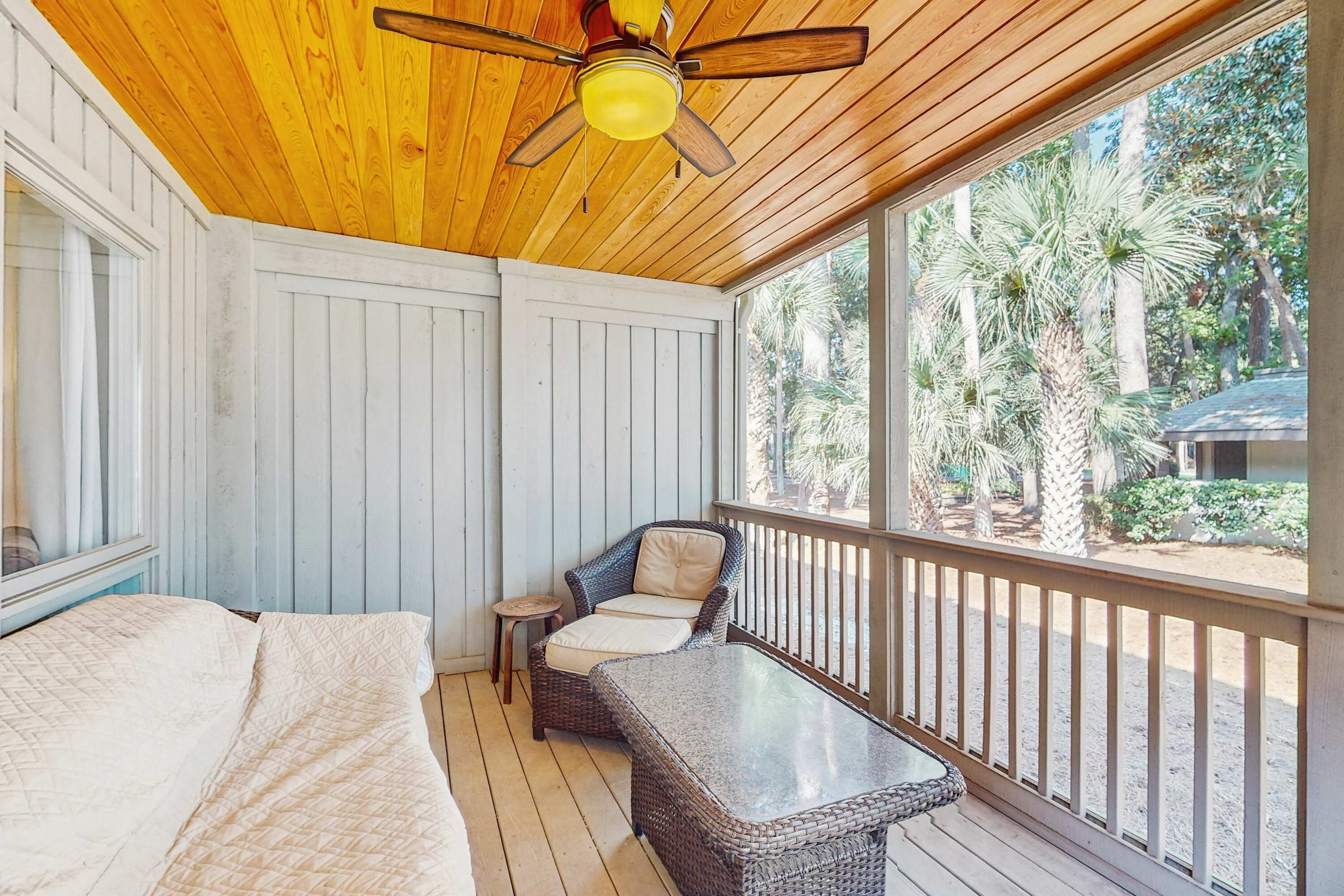 A room with a ceiling fan, a bed, a wicker chair, and a glass table.