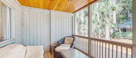 A room with a ceiling fan, a bed, a wicker chair, and a glass table.