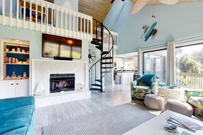 A spacious living area with a fireplace, a staircase, and a view to the outdoors.
