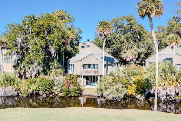 A house with a front porch, surrounded by trees and a pond.