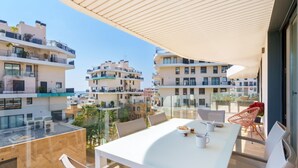 En modern balkong med ett vitt bord och stolar, med utsikt över ett bostadsområde med flera byggnader.
