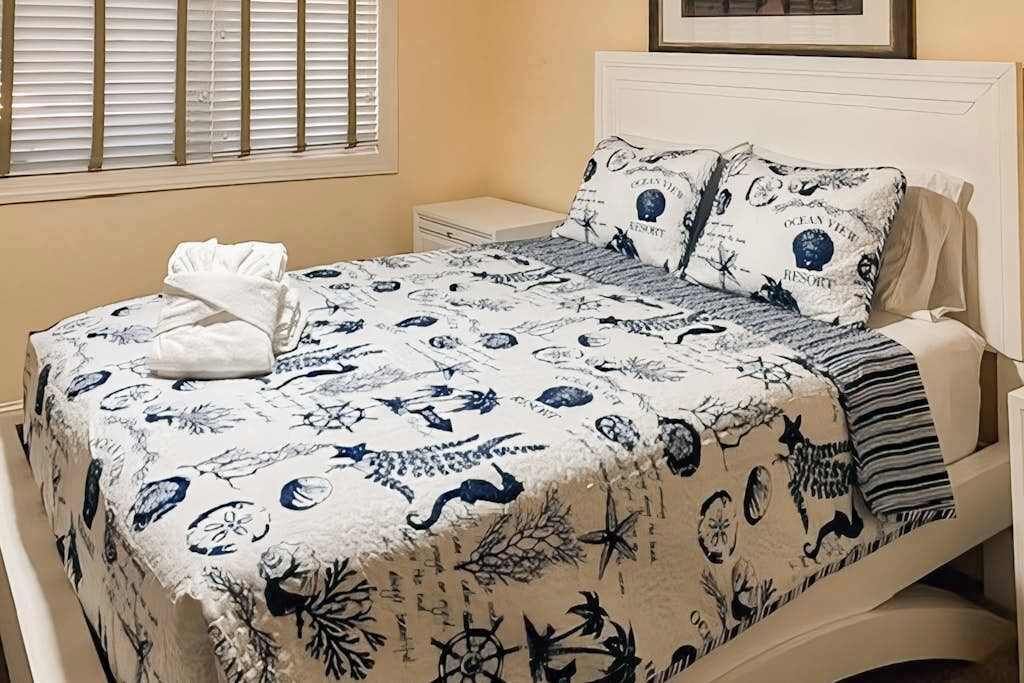 A bed with a nautical-themed bedspread, a white headboard, and a bedside table.