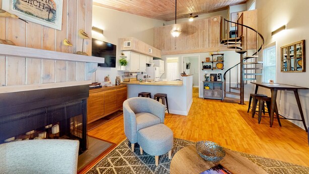 A spacious living area with a fireplace, a kitchen, a dining area, and a spiral staircase. - Driftwood Villa - 261 | Golf course-view condo with balcony, W/D, AC - dogs OK (Edisto Beach)