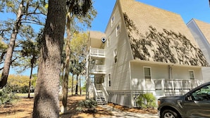 A two-story building with a balcony, a staircase, and a parked car. - Driftwood Villa - 261 | Golf course-view condo with balcony, W/D, AC - dogs OK (Edisto Beach)