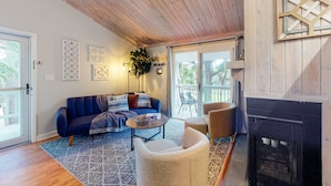 A cozy living room with a blue sofa, a white armchair, a coffee table, and a fireplace. - Driftwood Villa - 261 | Golf course-view condo with balcony, W/D, AC - dogs OK (Edisto Beach)