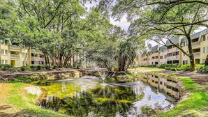 A tranquil courtyard with a central pond, surrounded by lush trees and multi-story buildings with balconies. - Private condo with sound views, effortless beach access, & resort amenities (Hilton Head)