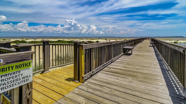A wooden boardwalk leading to a beach with a security notice sign. - Private condo with sound views, effortless beach access, & resort amenities (Hilton Head)