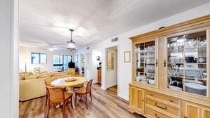 A dining area with a round table and chairs, a wooden cabinet with glass doors, and a sofa in the background. - Private condo with sound views, effortless beach access, & resort amenities (Hilton Head)