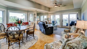 A spacious living area with a dining table, sofas, and chairs, large windows, and a ceiling fan. - Shorewood, Unit 530 Penthouse condo in Hilton Head with ocean views (Hilton Head)