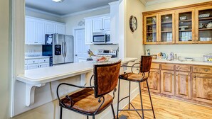 A kitchen with white cabinets, a microwave, a refrigerator, and a wooden cabinet with glass doors. - Beautiful home near the beach with beach access, central AC, & washer/dryer (Edisto Beach)