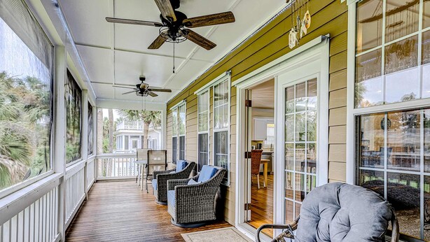 A covered porch with wicker furniture, a ceiling fan, and large windows. - Beautiful home near the beach with beach access, central AC, & washer/dryer (Edisto Beach)