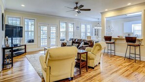 A spacious living room with a large sofa, two armchairs, a coffee table, and a TV. There are multiple windows, a ceiling fan, and a chandelier. - Beautiful home near the beach with beach access, central AC, & washer/dryer (Edisto Beach)