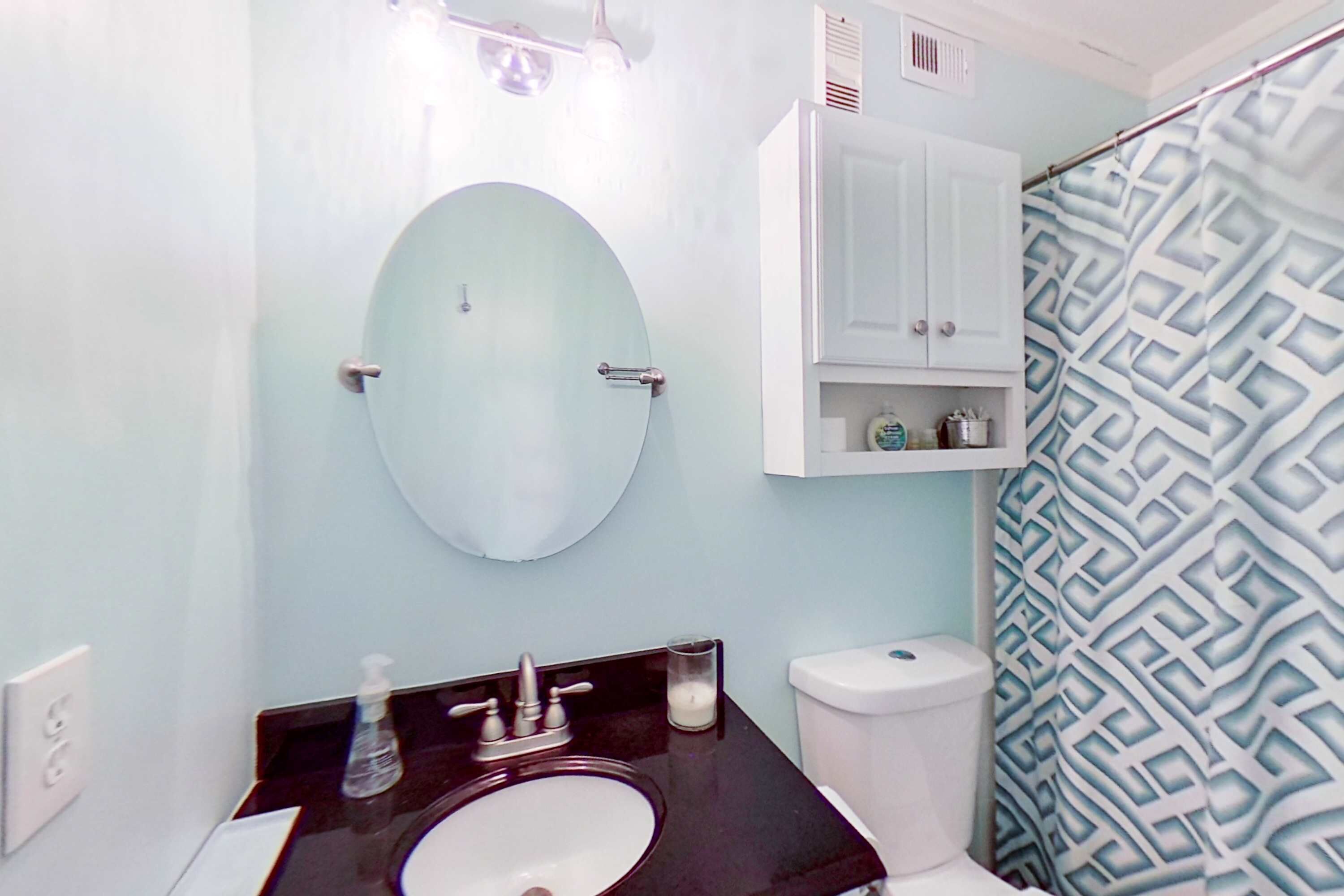 Une salle de bain avec un miroir rond, un lavabo, des toilettes et un rideau de douche.