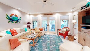 Ein Wohnzimmer mit Deckenventilator, einer Couch mit bunten Kissen, einem Couchtisch und einem gemusterten Teppich.