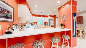 Eine moderne Küche mit weißer Arbeitsplatte, orangefarbenen Wänden und einer Bar mit Barhocker.