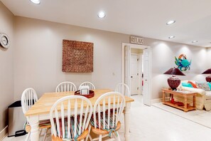 A dining area with a wooden table and white chairs, a woven wall hanging, and a decorative crab sculpture. - Family Friendly home near the Ocean w/Free WiFi, Sun deck, and Screened in Porch (Edisto Beach)
