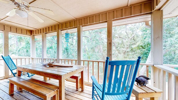 Eine Holzterrasse mit Tisch und Stühlen, großen Fenstern und einem Deckenventilator.