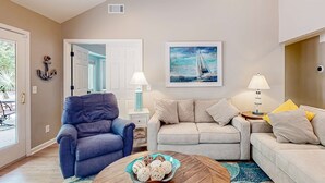 Un salon avec un fauteuil bleu, un canapé beige et une table basse ronde agrémentée d’objets décoratifs.