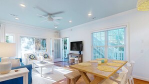 A spacious living room with a wooden dining table, white chairs, a ceiling fan, and a television. - Sea Sea Rider (Edisto Beach)