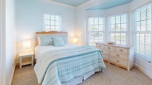 A bedroom with a bed, bedside lamps, a dresser, and a window with blinds. - Sea Sea Rider (Edisto Beach)