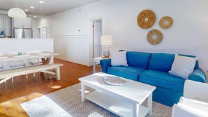A modern living room with a blue sofa, white coffee table, and a dining area with a wooden table and chairs. - Sea Sea Rider (Edisto Beach)