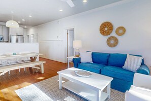 A modern living room with a blue sofa, white coffee table, and a dining area with a wooden table and chairs. - Sea Sea Rider (Edisto Beach)