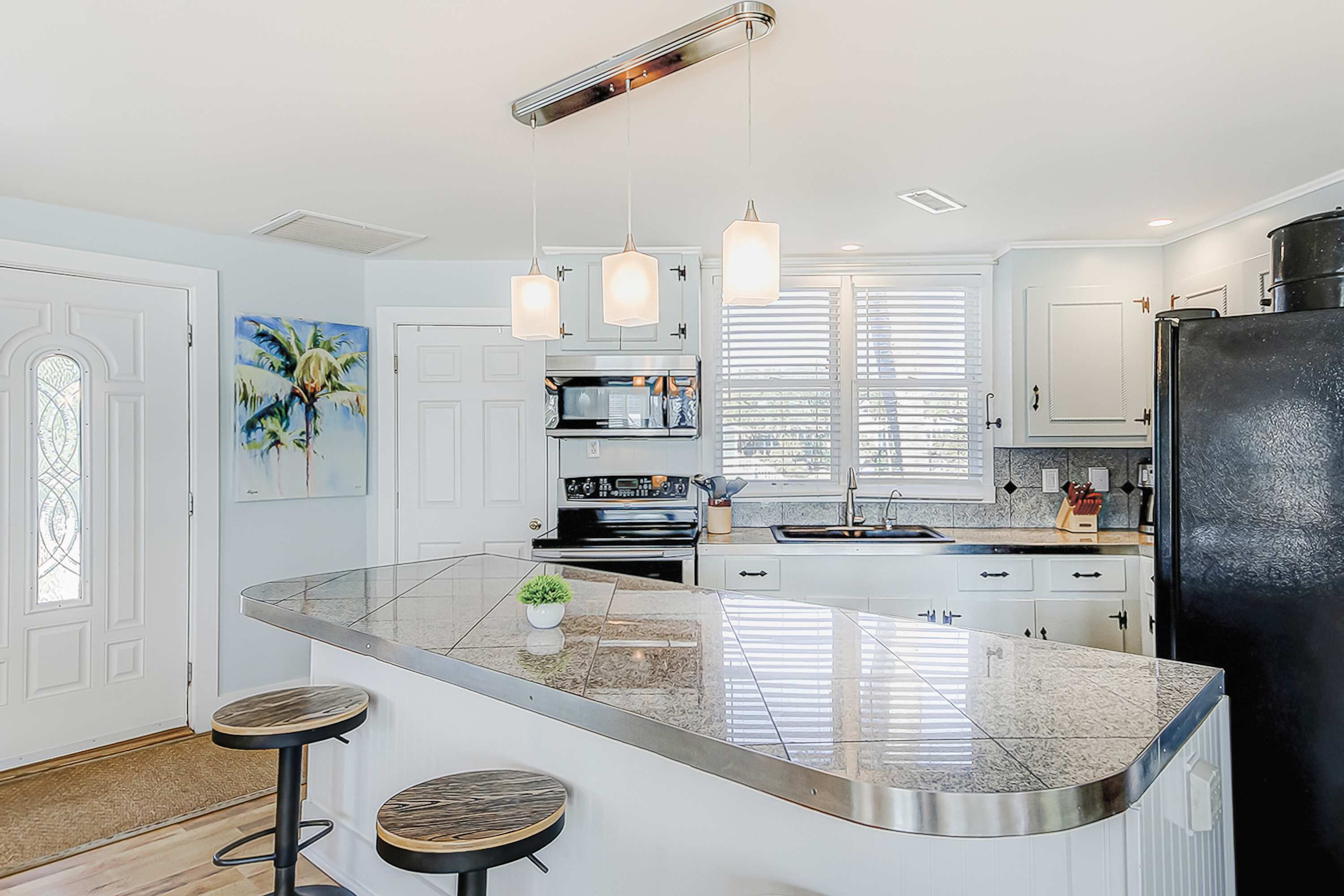 Een moderne keuken met een centraal eiland, hangende lampen en een koelkast.