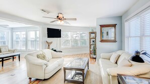 Un salon spacieux doté d’un ventilateur de plafond, de grandes fenêtres, d’un téléviseur à écran plat et d’une table basse moderne.