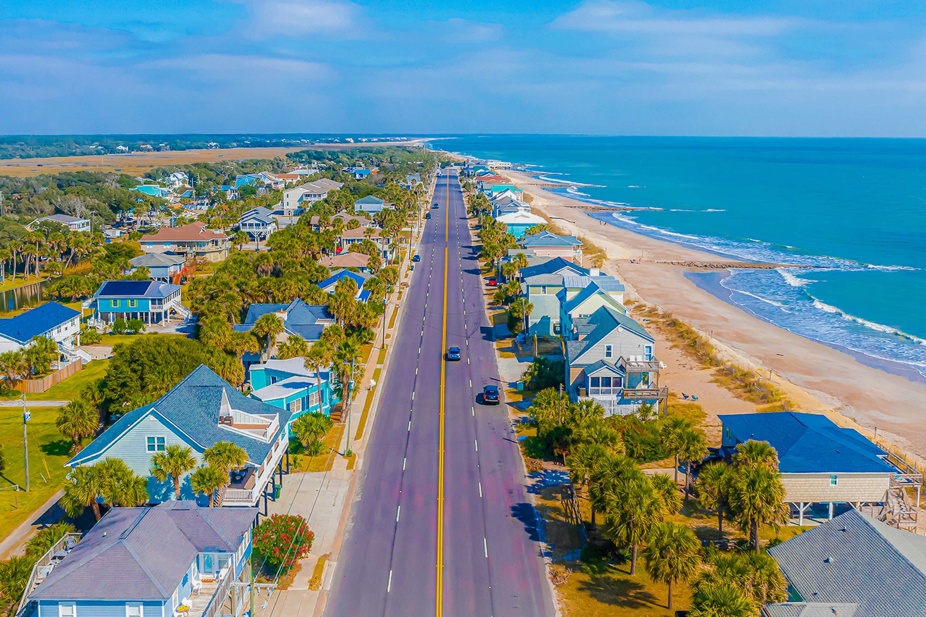 A coastal road lined with houses, a beach, and the ocean.