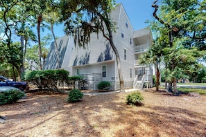 A two-story building with a white exterior, a front porch, and a small front yard with trees and shrubs. - 3rd-floor, dog-friendly condo with loft, balcony, free WiFi and golf course view (Edisto Beach)