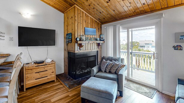 A cozy living room with a fireplace, wooden ceiling, and a balcony with a view. - 3rd-floor, dog-friendly condo with loft, balcony, free WiFi and golf course view (Edisto Beach)