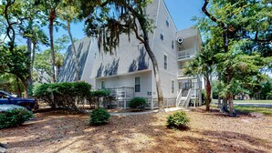 A two-story building with a balcony on the second floor, surrounded by trees and a well-maintained lawn. - 3rd-floor, dog-friendly condo with loft, balcony, free WiFi and golf course view (Edisto Beach)