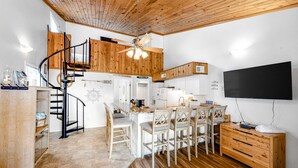 A modern kitchen with a wooden ceiling, a spiral staircase, and a dining area with white chairs. - 3rd-floor, dog-friendly condo with loft, balcony, free WiFi and golf course view (Edisto Beach)