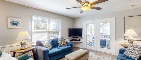 A living room with a ceiling fan, a television, and a patterned rug.