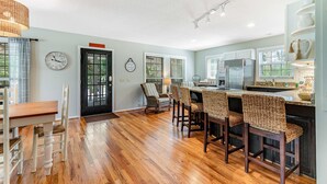 Uma cozinha ampla com piso de madeira, uma área de jantar com mesa e cadeiras de madeira, e uma geladeira moderna.