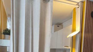 A compact room with a bed, a small table, a chair, and a curtain. - Le 4 Saisons (Ustou)