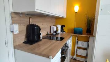 A compact kitchen with white cabinets, a wooden countertop, a coffee maker, a kettle, a toaster, and a small plant.