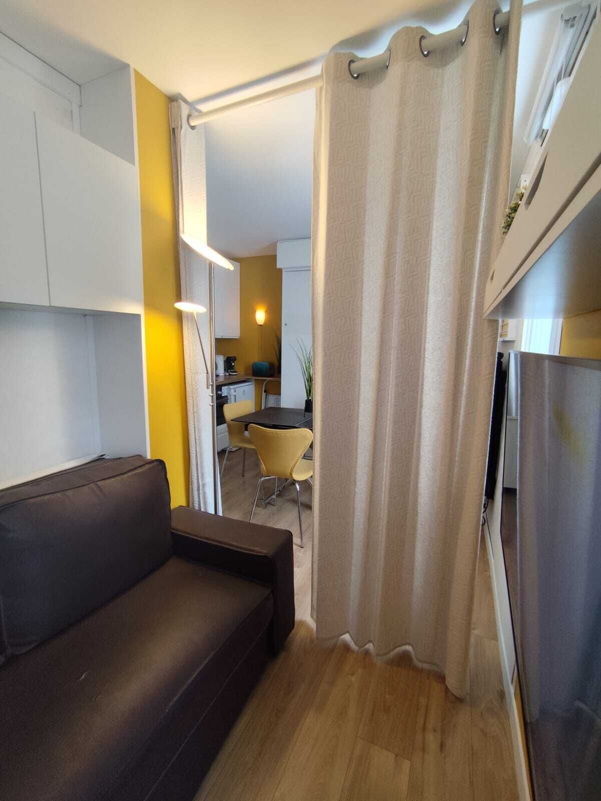A compact living space with a sofa, a dining area with chairs, and a kitchen in the background.