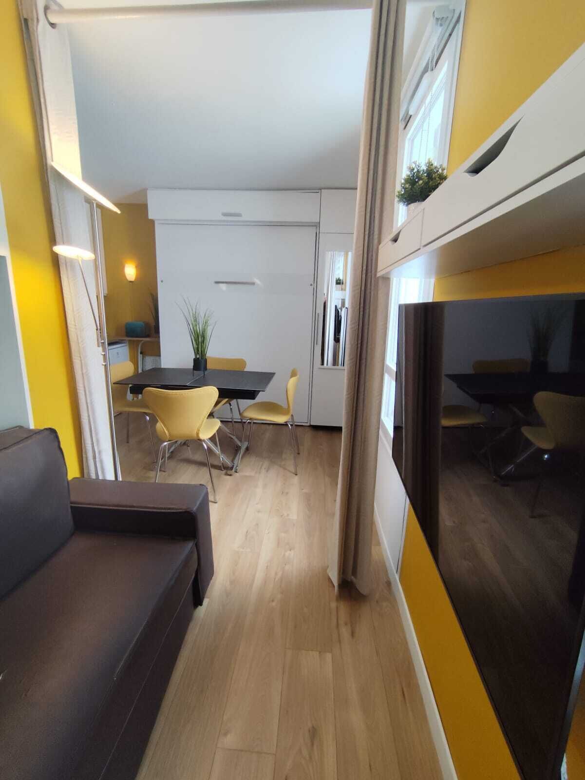 Una sala moderna con sofá, un comedor con sillas, una mesa y una cocina al fondo.