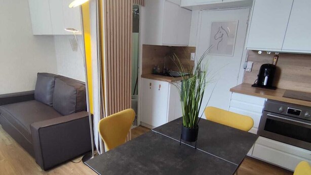 A modern kitchen with white cabinets, a dining table with yellow chairs, and a gray sofa in the living area. - Le 4 Saisons (Ustou)