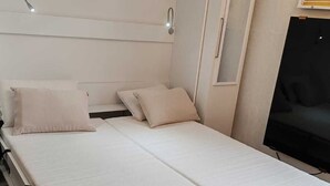 A single-bed room with a headboard, a bedside table, a lamp, and a TV. - Le 4 Saisons (Ustou)