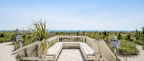 A wooden boardwalk leading to a beach with a clear view of the ocean.