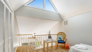 Een slaapkamer met dakraam, houten vloer, een stoel met kussen en twee bedden.