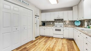 A kitchen with white cabinets, a tiled backsplash, and a wooden floor. - Bay view home three blocks to the beach with WiFi, central AC, and private w/d (Edisto Beach)