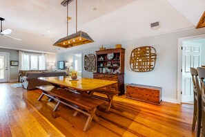Ein geräumiger Essbereich mit Holztisch und Bänken, einem Deckenventilator und einem Bücherregal mit Dekoration.