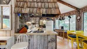 Una cocina rústica con paredes de madera, una isla central y un comedor con sillas amarillas.