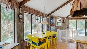 Un interior rústico de madera con una mesa y sillas amarillas, ventanas grandes y una lámpara colgante.