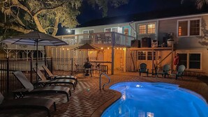 A swimming pool with lounge chairs, a covered seating area, and a two-story building with a balcony. - Ocean-view dog-friendly home across street from beach with private pool, W/D, AC (Edisto Beach)